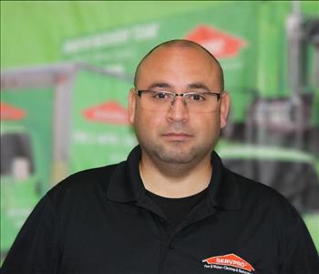 a man in a black shirt standing in front of a green SERVPRO truck