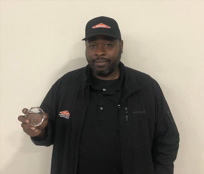 a man holding an award in front of a beige wall